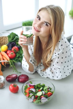 Diyet yapan bir kadın. Sağlıklı salata yiyen genç ve mutlu bir kadın yeşil taze malzemelerle masada oturuyor.