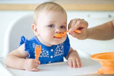 Bir anne bebeğini kaşıkla besler. Anne, sevimli bebeğine sağlıklı yiyecekler veriyor.. 