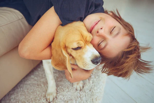 Happy boy and dog Beagle hugs her with tenderness, smiles, looks at the camera at home. Pets. Emotions of people. Childhood. Life style. Animal care.