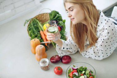 Diyet yapan bir kadın. Sağlıklı salata yiyen genç ve mutlu bir kadın yeşil taze malzemelerle masada oturuyor.