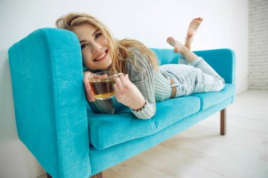 Evde bir kadın kanepede çay içiyor..