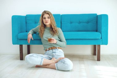 Güzel bir kadın evdeki kanepede çay içiyor. Genç kız kanepede yoga pozu veriyor..