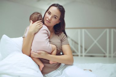 Genç bir anne yeni doğmuş bebeğini kucağında tutuyor. Emziren bir bebeğin annesi. Anne bebeğini emziriyor. Aile evdedir. Mutlu bir anne ve çocuğun portresi..