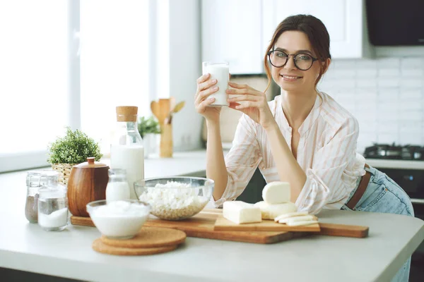 Young woman with milk, cottage cheese, sour cream, cheese in the kitchen at home indoors, beautiful girl sitting at the table, happy woman smile, natural organic.