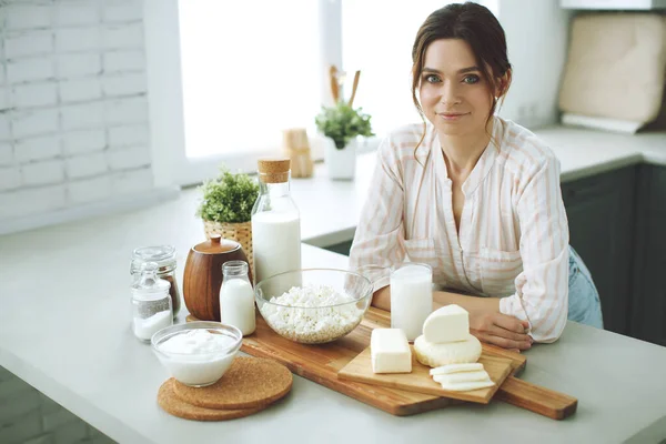 Young woman with milk, cottage cheese, sour cream, cheese in the kitchen at home indoors, beautiful girl sitting at the table, happy woman smile, natural organic.