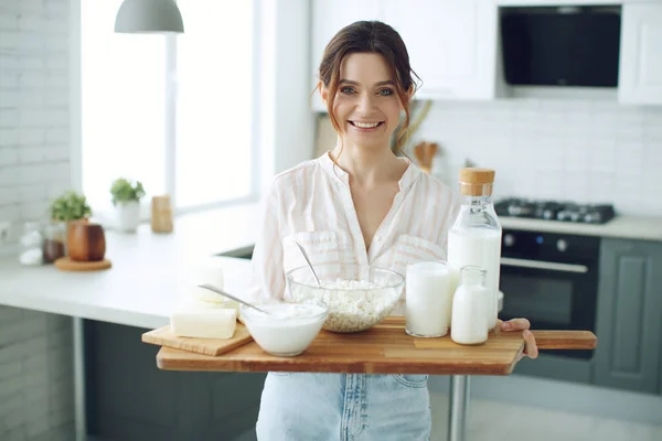 Fiatal nő tejjel, túróval, tejföllel, sajttal a konyhában otthon, gyönyörű lány ül az asztalnál, boldog nő mosolyog, természetes organikus. — Stock Fotó