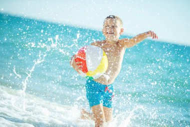 Çocuk denizde eğleniyor. Yaz, mutluluk, deniz ve çocuklu bir top.. 