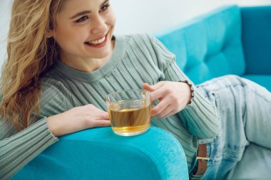 Genç bir kadın evde oturuyor ve çay içiyor..