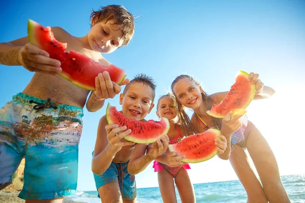 Kinder spielen am Meer und essen Wassermelone. — Stockfoto
