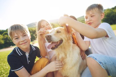 Çocuklar doğada köpekle oynarlar..