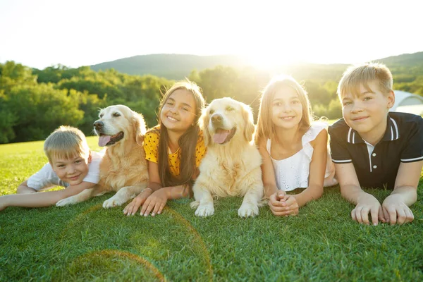 Group of happy children playing on green grass in a spring park with a dog. — Stock Photo, Image