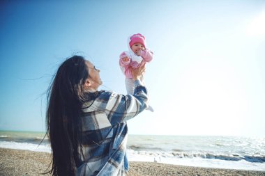 Deniz kenarında çocuklu bir kadın. Güzel anne deniz kenarında bebeğiyle oynuyor..