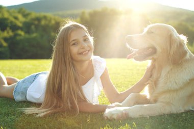 Şirin gülümseyen küçük kız, yaz parkında bir av köpeğine sarılıyor..