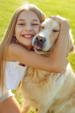 Şirin gülümseyen küçük kız, yaz parkında bir av köpeğine sarılıyor..
