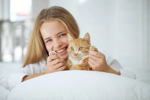 La chica está descansando en la cama con su gatito jengibre. Un niño con un animal. — Foto de Stock