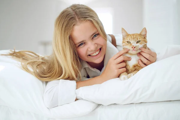 La chica está descansando en la cama con su gatito jengibre. Un niño con un animal. — Foto de Stock