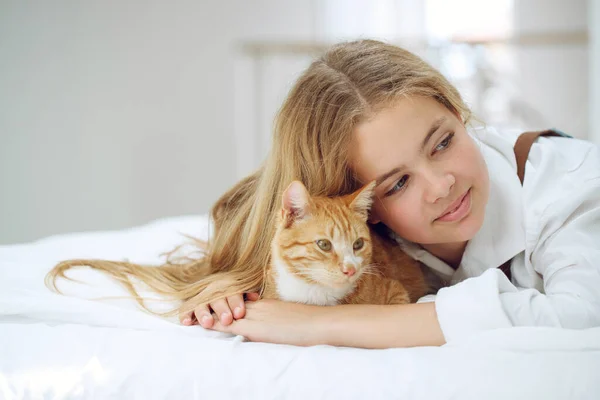 La chica está descansando en la cama con su gatito jengibre. Un niño con un animal. — Foto de Stock