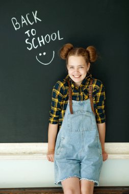 Mutlu gülümseyen kız. Tahtadaki çocuk. Arka planda yazı tahtası olan kapalı alan sınıfındaki kız. Okula dönüyoruz..