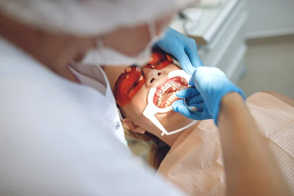 Tienermeisje met beugel op bezoek bij de orthodontist in de kliniek. Installatie van een beugelsysteem. — Stockfoto