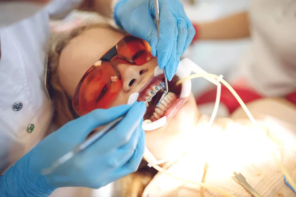 Tienermeisje met beugel op bezoek bij de orthodontist in de kliniek. Installatie van een beugelsysteem. — Stockfoto