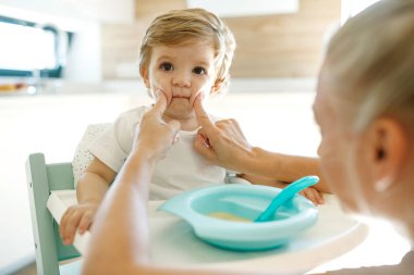 Annesi bebeği besliyor. Genç bir kadın bebeğini kaşıkla besliyor..