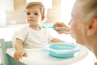 Annesi bebeği besliyor. Genç bir kadın bebeğini kaşıkla besliyor..