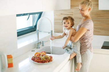 Çocuk ellerini yıkar. Annem küçük bir çocuğun ellerini yıkamasına yardım eder..