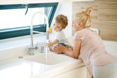 Çocuk ellerini yıkar. Annem küçük bir çocuğun ellerini yıkamasına yardım eder..