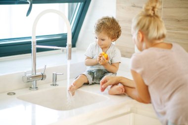 Çocuk ellerini yıkar. Annem küçük bir çocuğun ellerini yıkamasına yardım eder..