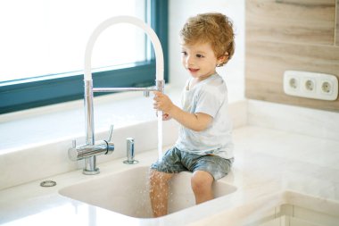 Çocuk ellerini yıkar. Küçük çocuk musluk suyuyla oynuyor..