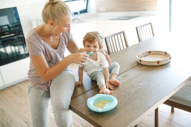 Annesi bebeği besliyor. Genç bir kadın bebeğini kaşıkla besliyor..
