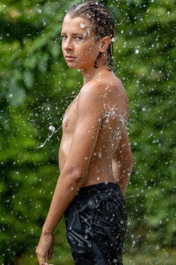 Genç bir erkek su sıçratıyor. Genç yakışıklı çocuk açık havada.