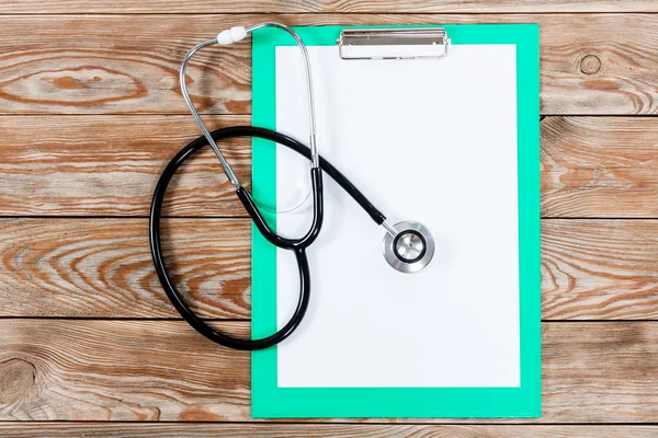 Medical clipboard and stethoscope on wooden table background.