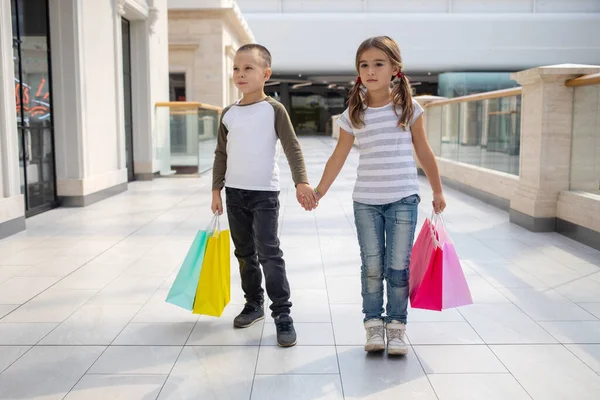 Grup portresi iki sevimli sevimli okul öncesi çocuk alışveriş gidiyor. Beyaz kız ve oğlan alışveriş merkezinde. Alışveriş torbaları tutan çocuklar.