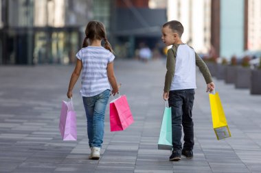 Grup portresi iki sevimli sevimli okul öncesi çocuk alışveriş gidiyor. Beyaz kız ve oğlan alışveriş merkezinde. Alışveriş torbaları tutan çocuklar.