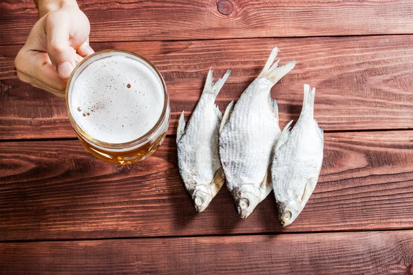 Mano con vaso de cerveza y pescado seco . — Foto de Stock