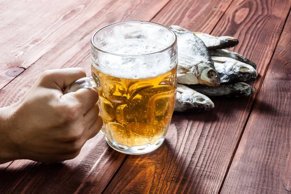 Mano con vaso de cerveza y pescado seco . — Foto de Stock