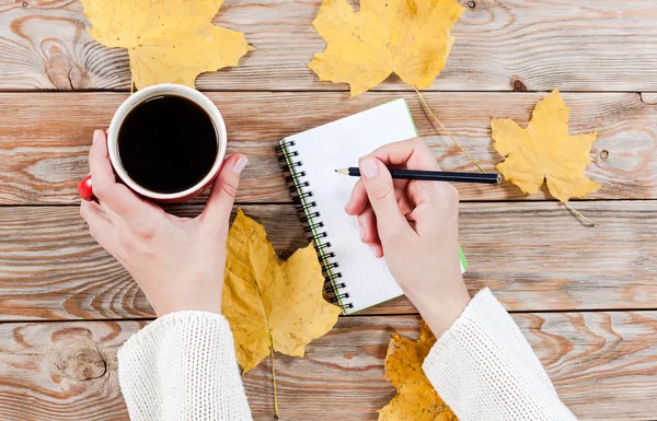 Mão feminina escrevendo em notebook perto de xícara de café — Fotografia de Stock