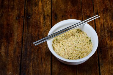 Beyaz kasede pişmiş erişte ve siyah ahşap masada paslanmaz çelik çubuklar yemeye hazır.