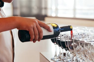 Akşam yemeği daveti için hazırlanan kırmızı şarabı şişeden şarap bardağına dolduran bir garson. Fotoğrafın arka pencerenin dışındaki güneş ışığından yansıyan parlak bir etkisi var..