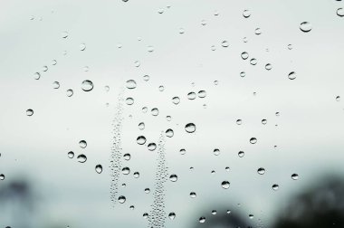 Yağmurlu bir günde yağmur damlaları pencerenin dışındaki bulanık arka planda su damlacıkları yüzeye akıyor.