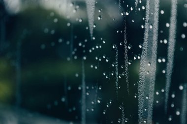 Yağmurlu bir günde yağmur damlaları pencerenin dışındaki bulanık arka planda su damlacıkları yüzeye akıyor.