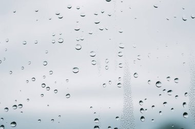 Yağmurlu bir günde yağmur damlaları pencerenin dışındaki bulanık arka planda su damlacıkları yüzeye akıyor.