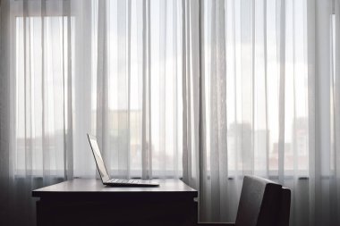 Büyük pencerenin yanındaki ahşap masanın üzerine koyulmuş bir defter. Büyük şehirdeki otel odasında ya da ofiste hiç kimse yoktu.