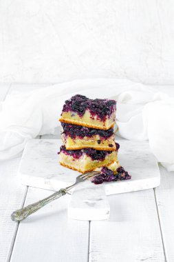 Beyaz mermer kesim tahtası ve beyaz ahşap masa üzerinde üç parça yaban mersinli kek.