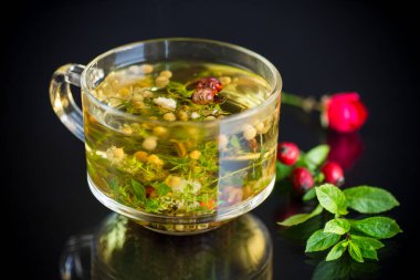 Siyah arka planda cam bardakta çeşitli bitkilerden sıcak bitki çayı.
