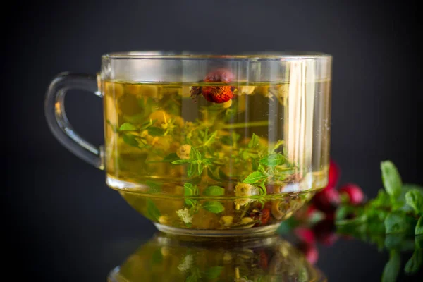 Hot herbal tea from various herbs in glass cup on black background — Stock Photo, Image