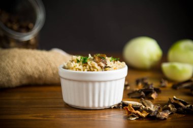 Kurumuş orman mantarlarıyla pişirilmiş pirinç, ahşap bir masada bir kase içinde.