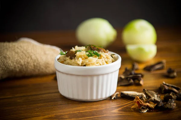 用干燥的森林蘑菇煮熟的米 放在木制桌子上的碗里 — 图库照片
