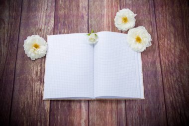 Güzel beyaz güller ve ahşap bir masada boş bir defter.